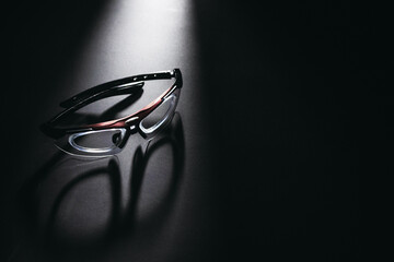 Stylish modern eyeglasses on dark reflective surface under spotlight