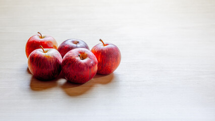 Five red apples arranged on light wooden surface with soft natural lighting