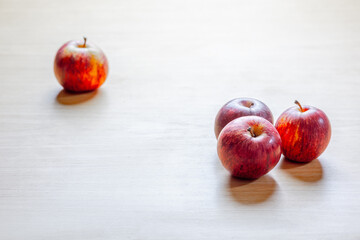 Four red apples on light wooden surface displaying artistic minimalism