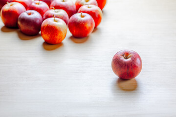 Single red apple standing out among group of similar apples on wooden surface
