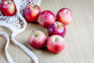 Fresh red apples on wooden surface with reusable cotton bag