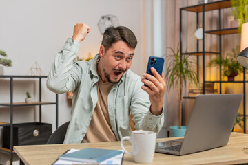 Happy young man using smartphone typing browsing saying yes, celebrating success victory, winning...