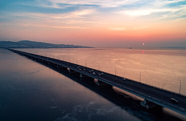 Aerial drone view of low-water bridge across the bay with moving car during the sunset. Active movement of transport cars vehicles in different directions.