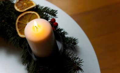 Close up of a burning candle on handmade advent wreath with natural spruce branches, dried oranges and rustic Christmas decoration symbolizing first Sunday of advent in warm cozy atmosphere