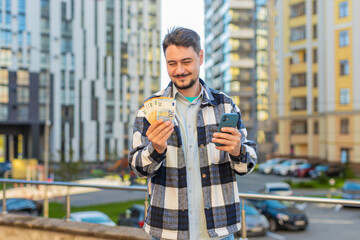 Happy rich mature Caucasian businessman tourist using smartphone and counting money euro cash...