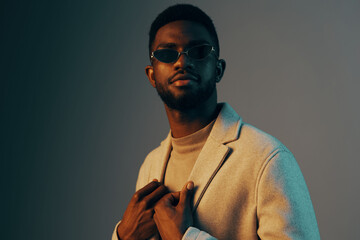 Stylish young man in sunglasses presenting a confident manner against a soft gradient background,...