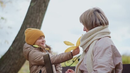 woman sits bench working laptop outdoors in autumn park among colorful leaves, little girl approaches offering golden foliage to distract mother who gently shifts hand aside before child steps back - Powered by Adobe