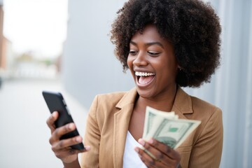 Excited Black Woman Looking at Phone and Holding Cash