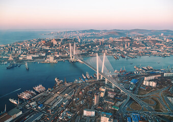 Obraz premium Aerial cityscape of Vladivostok at sunset showcasing urban development and the famous bridge connecting urban areas
