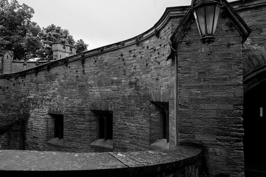 Atmospheric black and white shot of an ancient European castle wall with gothic architecture, medieval windows, and a classic lantern