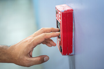 Activate fire alarm trigger system which is installed on building wall. Human action scene photo,...