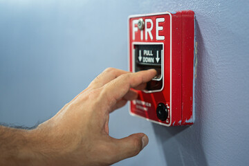 Activate fire alarm trigger system which is installed on building wall. Human action scene photo,...