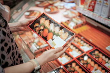 Person holding a box of assorted sushi in a supermarket