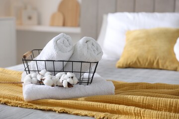 Clean towels, metal basket and cotton flowers on bed linens at home, closeup