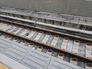 close-up, diagonal view of a modern train track. The parallel metal rails are secured to concrete...