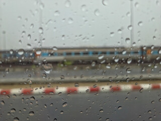 Rain-covered window view with blurred background showing a red-and-white barrier and a...