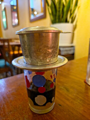 A Vietnamese coffee filter (phin) sits atop a glass with a small amount of condensed milk on a...