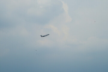 Twin-engine regional jet flying upward with landing gear retracted against a cloudy, hazy sky.