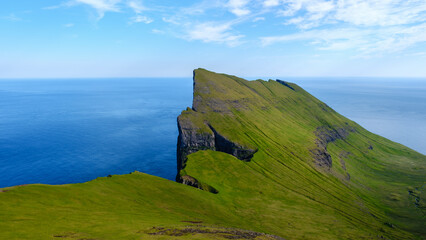 Majestic Mylingur cliffs rise sharply from the sparkling waters of the North Atlantic Ocean in the Faroe Islands.