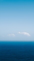 Serene and tranquil minimalist seascape featuring the deep blue ocean meeting a clear sky with a single wispy cloud on the horizon