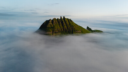 A dramatic peak in the Faroe Islands rises majestically above a blanket of mist, showcasing vibrant...