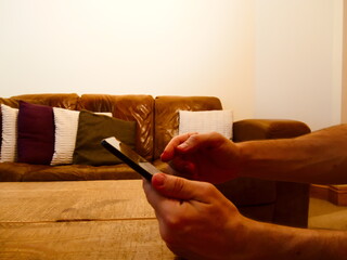 Man using phone in a living room with brown settee or couch in the background