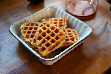 Close-up of freshly baked golden brown croffles served in a ceramic dish on a wooden table. A glass coffee pot and enamel mug complete the cozy breakfast setup.
