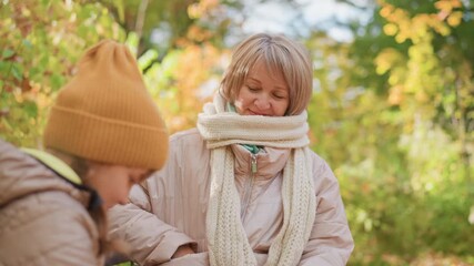 mother wearing scarf pulls fruit from pocket as daughter in orange beanie watches with bowed head, emotional warmth and quiet comfort exchange between parent and child