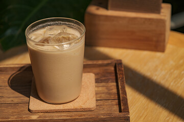 a glass of iced milk coffee on wooden table in sun light and shade