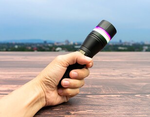 Hand holding a black flashlight against a blurred cityscape backdrop