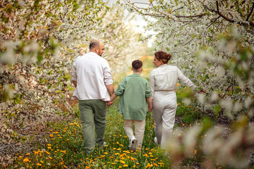 Happy family mom dad and teenager boy having fun on a spring walk in a blooming park