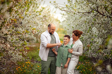 Happy family mom dad and teenager boy having fun on a spring walk in a blooming park