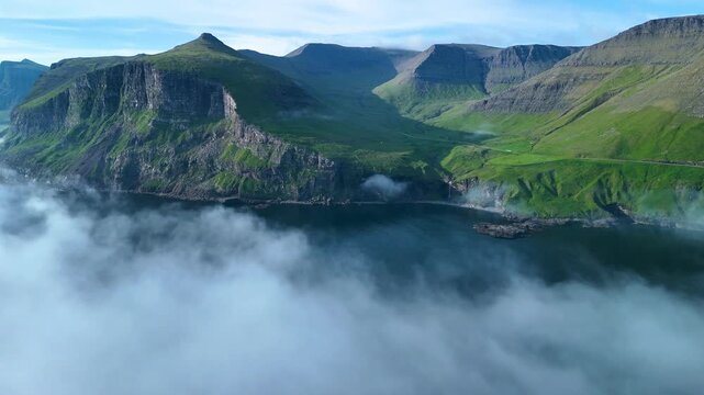 Explore the breathtaking cliffs and serene waters of the Faroe Islands, where dramatic rock formations rise above foggy shores, creating a captivating and tranquil atmosphere throughout the day.