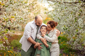 Happy family mom dad and teenager boy having fun on a spring walk in a blooming park