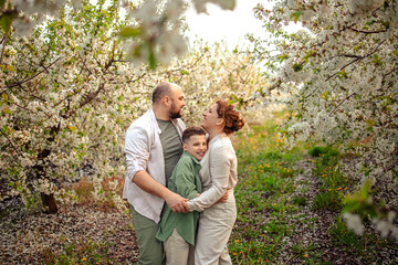 Happy family mom dad and teenager boy having fun on a spring walk in a blooming park