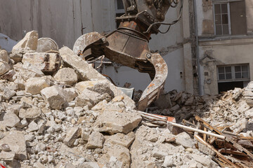 Un engin de destruction avec des pinces en train de prendre des gravats d'un bâtiment. 