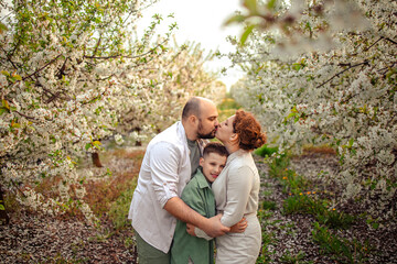 Happy family mom dad and teenager boy having fun on a spring walk in a blooming park