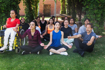 Group of latin sporty people meditating next to mexican woman in wheelchair outdoors in Mexico Latin America. Hispanic diverse group in inclusion concept, disabilities and disabled person doing yoga