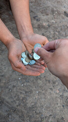 A hand places coins into the hands of a beggar receiving alms on the street.
