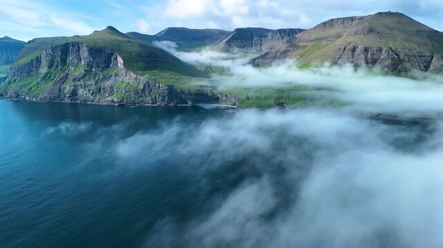 Witness stunning landscapes at Drangarnir cliff, where towering cliffs meet the North Atlantic Ocean. Misty clouds roll over the verdant hills, creating an enchanting atmosphere of the Faroe Islands