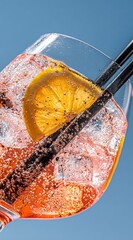 Refreshing orange cocktail. Effervescent liquid, ice cubes, and a lemon slice fill a glass with black straws against a bright blue background