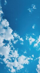 A clear blue sky speckled with scattered, fluffy white clouds on a bright day. High-angle, natural lighting