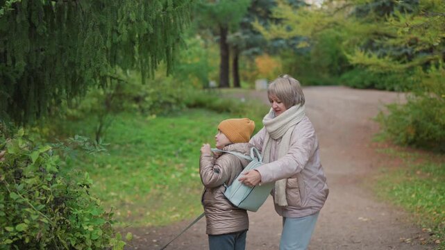mom adjusts daughter bag strap while guiding dog walk home on leafy trail, bundled in jackets and scarf under soft autumn light, intimate family moment showcasing care and togetherness