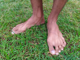 Bare feet of a person on green grass, close-up, low-angle shot. Man's feet standing on a lawn outdoors. A pair of feet on fresh green grass
