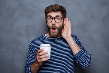 Shocked man with coffee trying to listen and eavesdrop on unbelievable office gossip