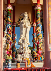 Large statue of Guanyin in colorful temple with dragon columns during sunny afternoon. Sriracha, Thailand.