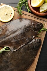Fresh raw flounder fish and spices on black wooden table, flat lay. Seafood