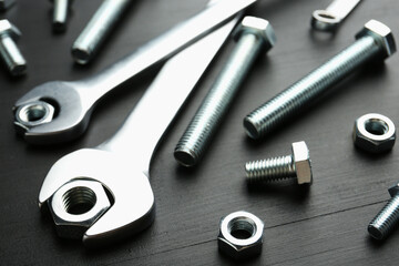 Many metal wrenches, bolts and nuts on black wooden table, closeup