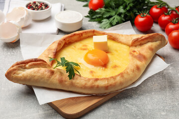Tasty khachapuri with cheese, egg, parsley and other products on light grey background, closeup