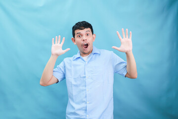 Surprised Man Expressing Shock and Excitement with Hands Raised Against a Soft Blue Backdrop